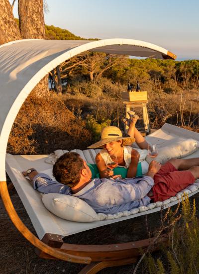 Relaxed couple in hammock, enjoying wine, vineyard view.