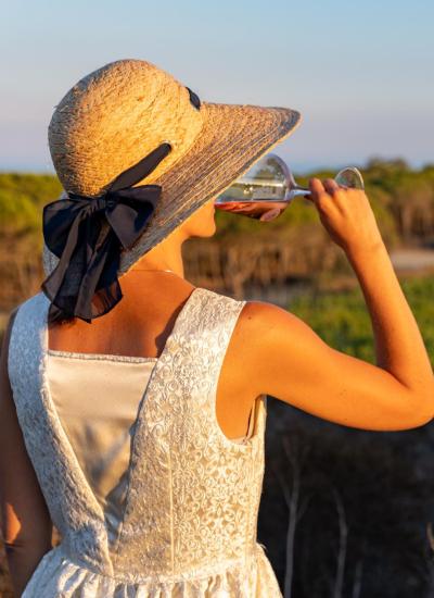 Donna beve vino in un vigneto al tramonto.