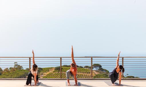 Tre persone fanno yoga all'aperto con vista sul mare.