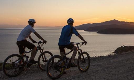 Due ciclisti ammirano il tramonto sul mare.