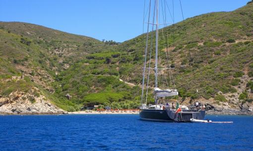 Barca a vela ormeggiata vicino a una spiaggia con colline verdi.