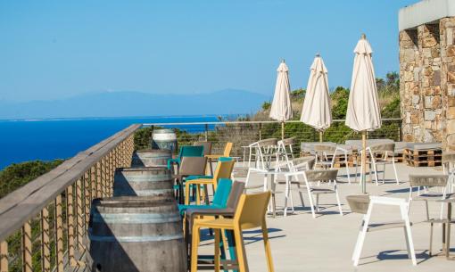 Terrazza panoramica con vista mare, sedie colorate e ombrelloni chiusi.