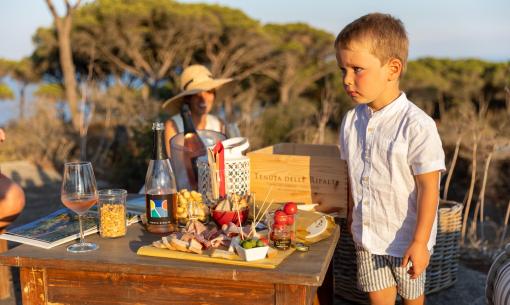 Bambino accanto a tavolo con cibo e bevande all'aperto.