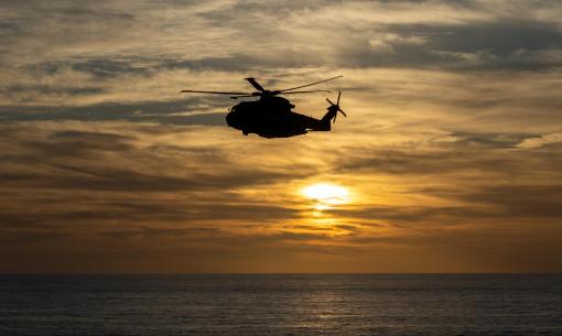 Helicopter flying at sunset over the sea.