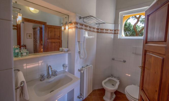 Bagno con bidet, lavandino e specchio, vista su albero.